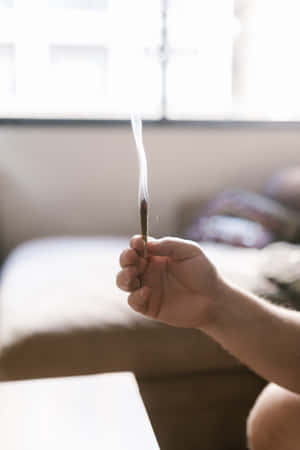 A Hand Holds A Freshly Lit Weed Blunt, Smoke Slowly Curling Around It. Wallpaper