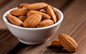 A Handful Of Almonds In A White Ceramic Bowl Wallpaper