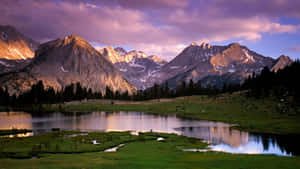 A Lake Surrounded By Mountains And Grass Wallpaper