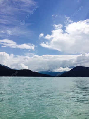 A Lake With Mountains And Clouds In The Background Wallpaper