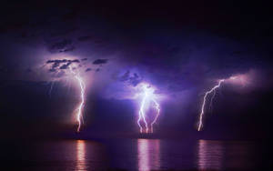 A Lightning Bolt Illuminates The Night Sky Near The Ocean. Wallpaper