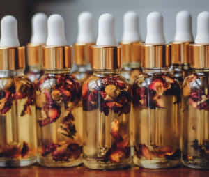 A Luxurious Bottle Of Rose Oil With Fresh Pink Roses Wallpaper