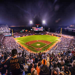 A Majestic Baseball Stadium Illuminated Under A Dazzling Evening Sky Wallpaper