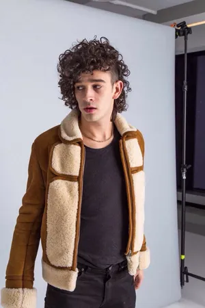 A Man In A Brown Shearling Jacket Standing In Front Of A Camera Wallpaper