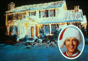 A Man In A Santa Hat Is Standing In Front Of A House With Lights Wallpaper