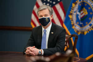 A Man In A Suit Sitting At A Desk Wearing A Face Mask Wallpaper