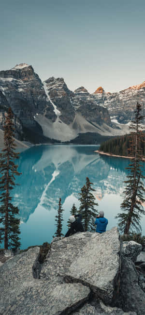 A Man Is Sitting On A Rock Overlooking A Lake Wallpaper