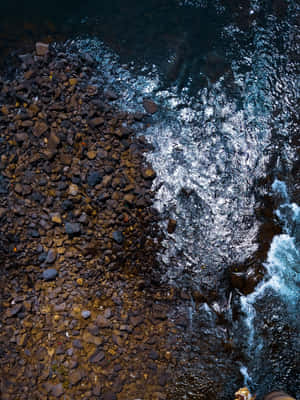 A Man Is Standing On A Cliff Overlooking The Water Wallpaper