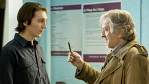 A Man Is Talking To Another Man In A Hallway Wallpaper