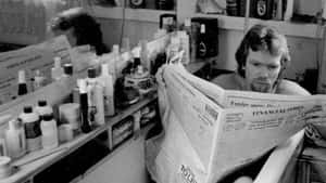 A Man Reading A Newspaper In A Bathroom Wallpaper