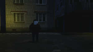 A Man Standing In A Dark Street At Night Wallpaper