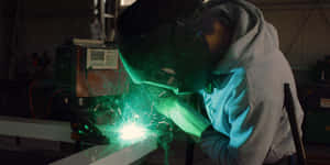 A Man Welding Metal In A Factory Wallpaper