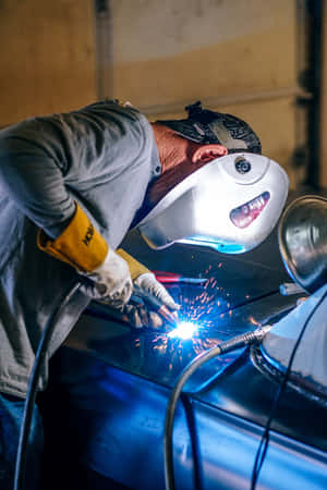 A Man Welding On A Blue Car Wallpaper