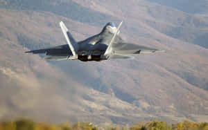 A Military Jet Flying Over A Mountain Wallpaper