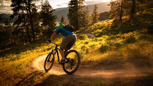 A Mountain Biker Racing Downhill Against The Backdrop Of A Breath-taking Sunset. Wallpaper