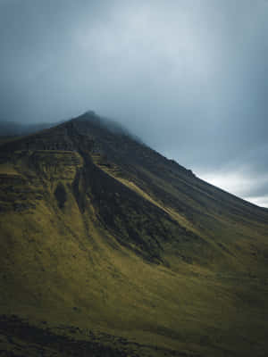 A Mountain Covered In Clouds With Grass And Grass Wallpaper