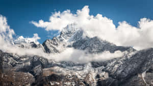 A Mountain Range Covered In Snow With Clouds Above It Wallpaper