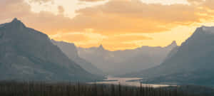 A Mountain Range With Trees And A River In The Background Wallpaper