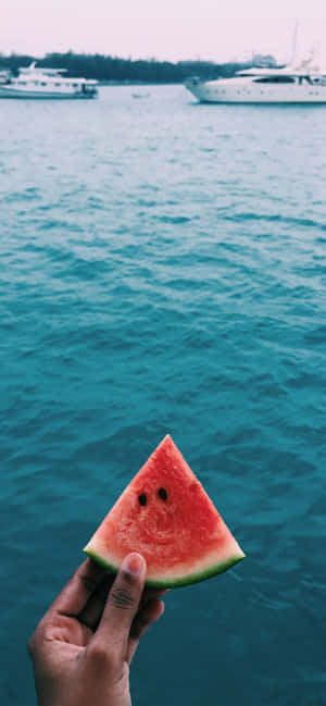 A Person Holding A Slice Of Watermelon In Front Of A Boat Wallpaper