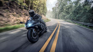 A Person Riding A Motorcycle Down A Road In The Forest Wallpaper