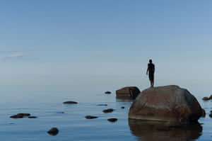 A Person Standing On A Rock In The Water Wallpaper