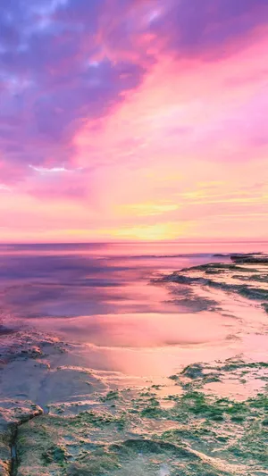 A Pink And Purple Sunset Over The Ocean Wallpaper