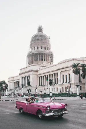 A Pink Convertible Driving Down The Street In Front Of A Building Wallpaper