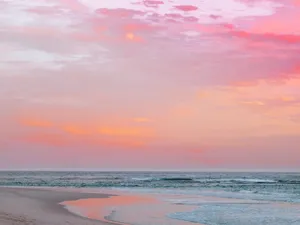 A Pink Sunset Over A Beach With Waves Wallpaper