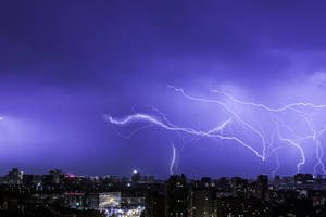 A Powerful Lightning Strike Illuminates The Night Sky Of A Big City Wallpaper