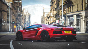 A Red Sports Car Driving Down A City Street Wallpaper