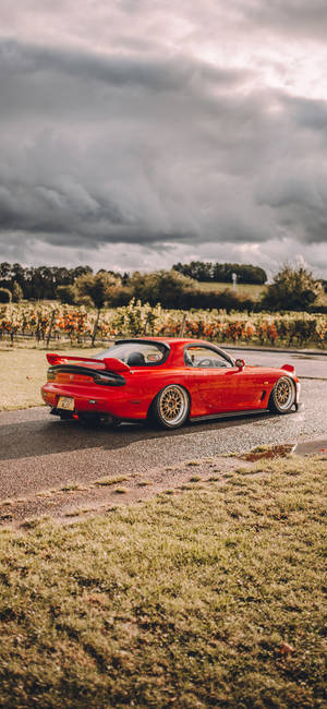 A Red Sports Car Driving Down A Road Wallpaper