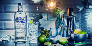 A Refreshing Scene Featuring A Bottle Of Absolut Vodka, A Lemon, And A Light Bulb. Wallpaper