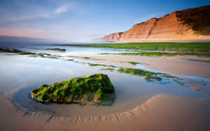 A Rock On The Beach With A Cliff In The Background Wallpaper