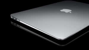 A Silver Macbook Pro Is Shown On A Black Surface Wallpaper