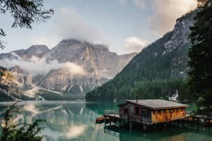 A Small Cabin Sits On A Dock In A Lake Wallpaper