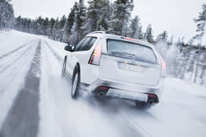 A Snowy Winter Road With A Car Driving Through The Picturesque Landscape Wallpaper