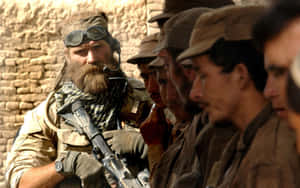 A Soldier With A Rifle In Front Of A Group Of Men Wallpaper