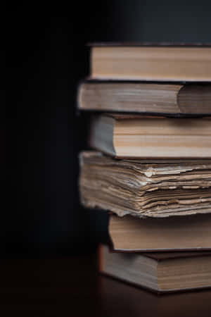 A Stack Of Books On A Table With A Dark Background Wallpaper