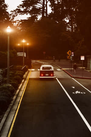 A Street With A Car Driving Down It Wallpaper