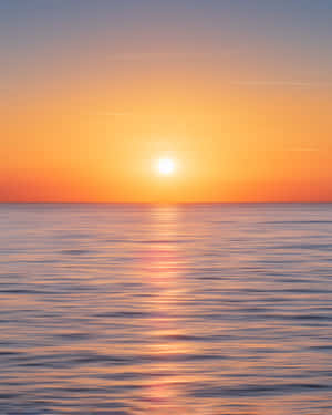 A Stunningly Beautiful Sunset Over The Calm And Inviting Ocean. Wallpaper