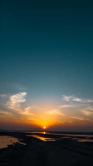 A Sunset Over A Beach With Water And A Boat Wallpaper