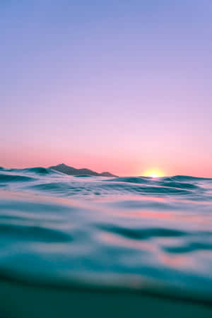 A Sunset Over The Ocean With Waves And Mountains Wallpaper