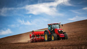 A Tractor Plowing A Field With A Blue Sky Wallpaper