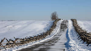 A Tranquil Snowy Road Through A Serene Winter Landscape Wallpaper