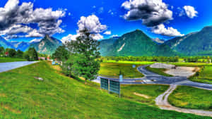 A View Of A Mountain Road And A Green Field Wallpaper