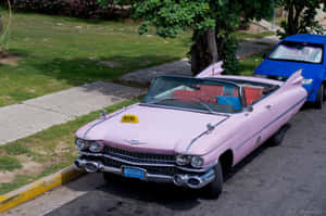 A Vintage Pink Cadillac Parked On The Street With A Beautiful Golden Sunset In The Background Wallpaper