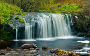 A Waterfall In A Forest With Rocks And Trees Wallpaper