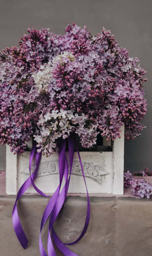 A White Crate With Purple Flowers And A Ribbon Wallpaper