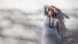 A Woman In A Gray Dress Leaning Against A Wall Wallpaper