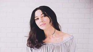 A Woman In A Gray Top Standing In A Bathroom Wallpaper